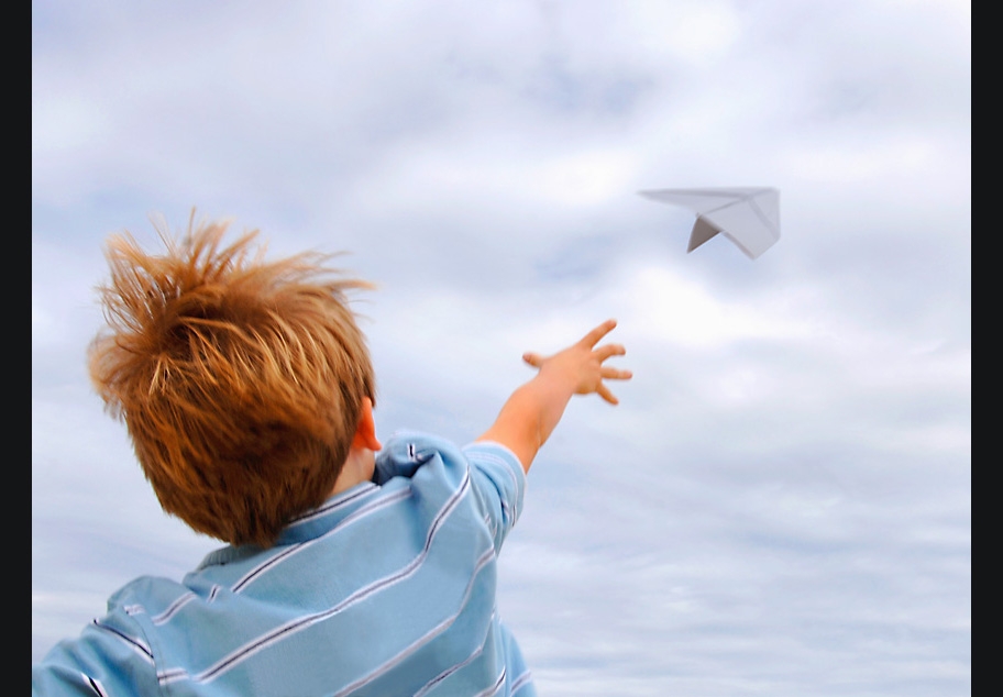Young boy flying paper airplane
